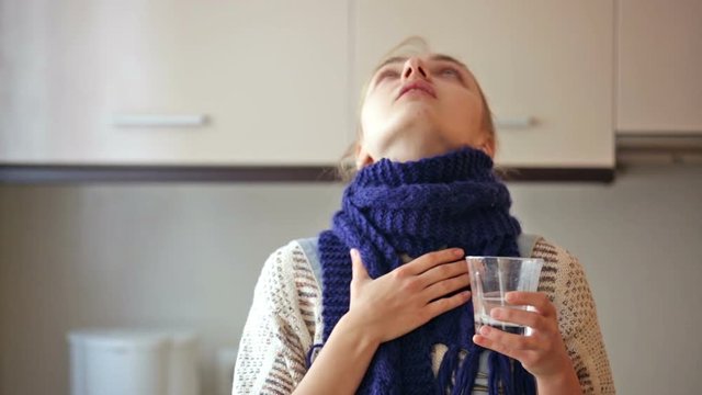 Girl with quinsy taking medicine and gargling throat in kitchen