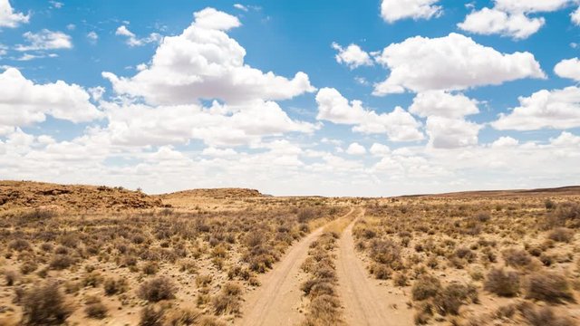 A scenic daytime drive time lapse on a gravel road with two dirt tracks in a grassy landscape setting with a blue sky and scattered clouds, front point of view 