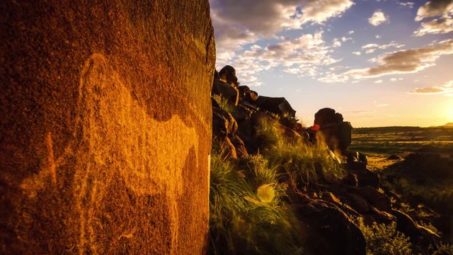 Static timelapse with a textured rock and a bushmen engraving on a hill with green grass in the foreground and the sun setting in the background with clouds moving towards the camera available on request.