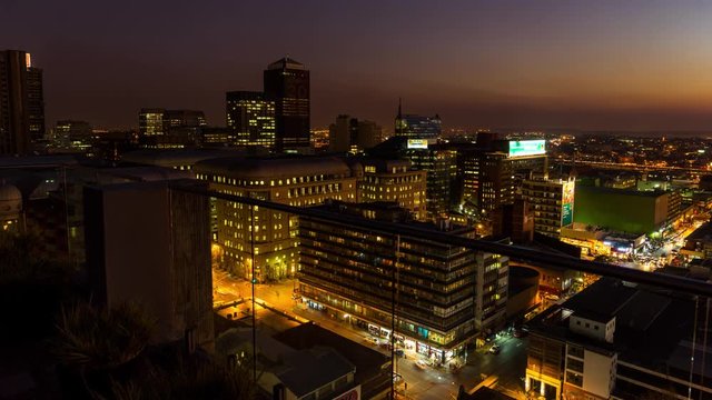 Medium timelapse at nightfall showing the view from a rooftop balcony across New Town. Jeppes town and the city centre of Johannesburg during peak traffic with the hustle and bustle of people in the streets, buildings and taxis, South Africa