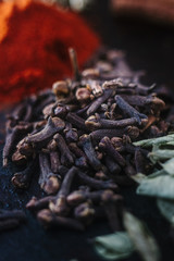 Black cloves spice over black plate surrounded by spices.