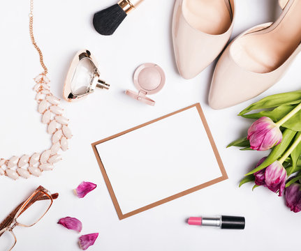 Woman's accessories of beige color, pink tulips and blank paper on white table
