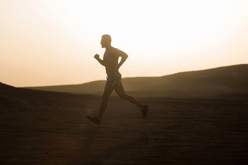 Fototapeta na wymiar Man runner running in dune at sunset