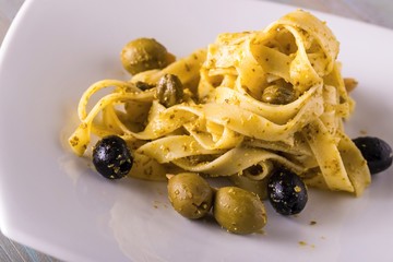 Portion of tagliatelle with green pesto and capers and olives