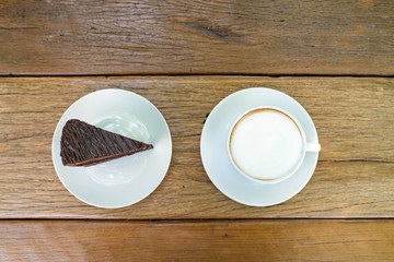 Top view shot : Cup of coffee and piece of chocolate cheesecake on wooden background.