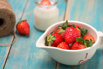 Bowl with fresh strawberry on blue wooden table.
