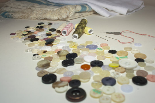 Reels of thread  in the middle of random buttons with the fabric on the background.
