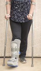 Unrecognisable woman wearing a medical orthopaedic boot with cruches