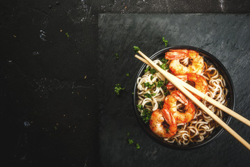 Asian soup with noodles (ramen), with miso paste, soy sauce, greens and shrimps prawn. On a black stone table, with chopsticks. Copy space top view