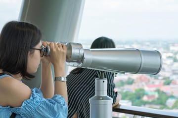 Woman looking in binoculars enjoying view above clouds during hiking trip - Telescope on the tower.