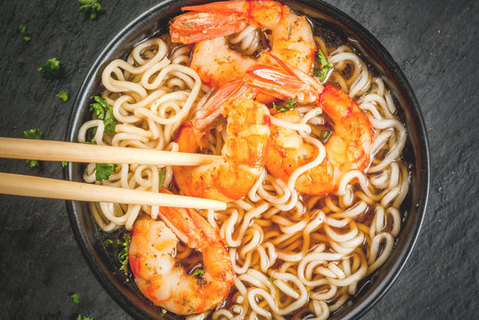 Asian soup with noodles (ramen), with miso paste, soy sauce, greens and shrimps prawn. On a black stone table, with chopsticks. Copy space top view
