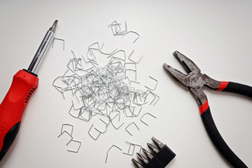 Pliers, screwdriver and staples on a white table, top view