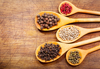 Black, white and red peppers in a wooden spoons