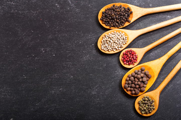 Black, white and red peppers in a wooden spoons