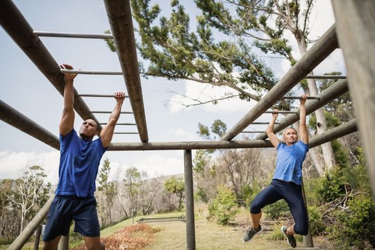 Fit man and woman climbing horizontal bars during obstacle course