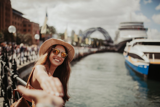 Woman in sunglasses holding boyfriend hand, while taking a photo of her, in Sydney Harbour.
