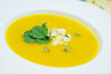 Ready-made pumpkin soup with blue cheese and greens in a plate. Healthy and tasty food with vitamins. Soft focus and close-up.