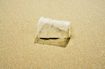 Fototapeta na wymiar Plastic cup on the sandy beach