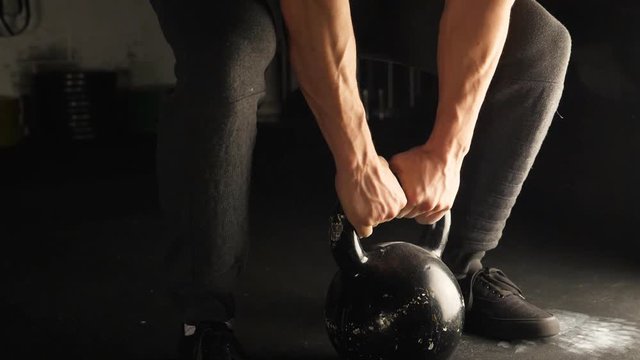 Slo-mo shot. Closeup of man's hands lifting kettlebell. Three quarter view.

