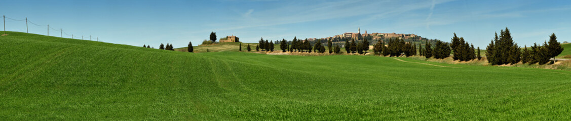 Fototapeta na wymiar PIENZA, TUSCANY / ITALY - MAR 31, 2017: beautiful landscape, with green rolling hills and tuscan cypress trees with Medieval Village of Pienza on background. Located in Siena countryside. Italy.