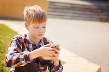 Child playing phone outdoors in sunny day.