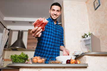 young man preparing meat in her kitchen , looking into the frame