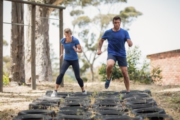 Man and woman running over the tire during obstacle course - Powered by Adobe