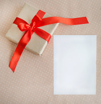 Holiday Post card. Gift box with red ribbon, a sheet of paper. Copy space Beige fabric background 