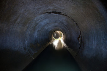 A stream of dirty, turbid waste water in a round sewer tunnel under Voronezh