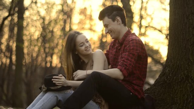 A girl and a guy are resting in the park, kissing, hugging, laughing On the Sunse