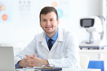 Young doctor with laptop sitting at table in office