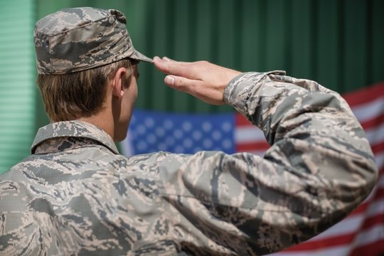 Rear view of military soldier giving salute to American flag
