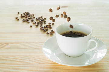 Coffee beans jumping into a white coffee cup on the wooden table