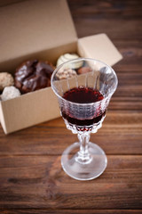 Glass of red wine and box with assorted sweets on wooden table closeup