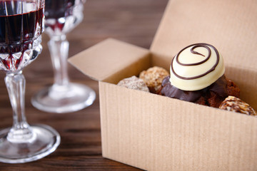 Box with assorted sweets and glasses of wine on wooden table closeup