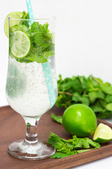 Fresh mojito cocktail with mint leaves, lime and straw on wooden background. Selective focus