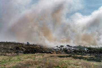 Fire at landfill with white smoke in sunny weather and clouded sky.