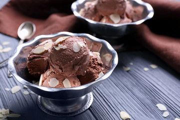Tasty ice-cream with almond slices in bowl on wooden background