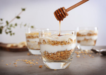 Pouring honey into glass with tasty yogurt dessert on table