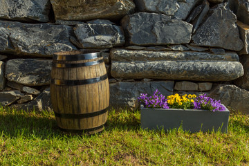 Vintage oak barrel on the grass with stone wall and pot of flowers