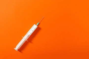 Syringe filled with a white liquid placed on a orange background. Isolated