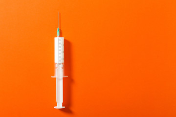 Syringe filled with a white liquid placed on a orange background. Isolated