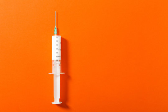 Syringe filled with a white liquid placed on a orange background. Isolated