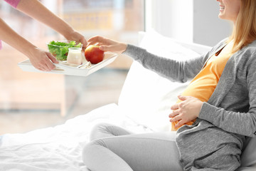 Female hands with breakfast for young pregnant woman resting on bed