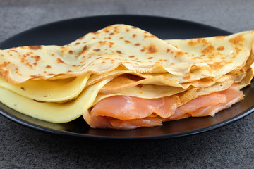 Two pancakes with salmon and cheese on black plate.