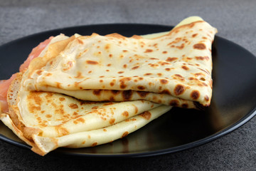 Two pancakes with salmon and cheese on black plate.