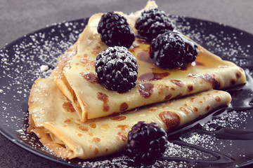 Pancakes with blackberries and honey on a black plate.