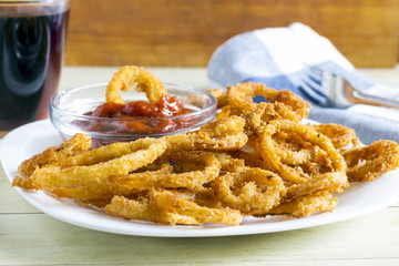 Crunchy fried onion rings and sauce on light wood background