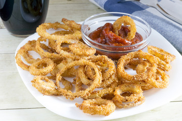 Crunchy fried onion rings and sauce on light wood background