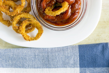 Crunchy fried onion rings and sauce on light wood background